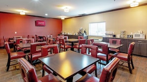 Un espace de restauration d’hôtel avec des chaises et des tables en cuir rouge, un coin cuisine équipé d’appareils électroménagers, et un panneau indiquant que le Wi-Fi est gratuit dans toutes les chambres.