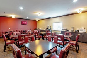 Un espace de restauration d’hôtel avec des chaises et des tables en cuir rouge, un coin cuisine équipé d’appareils électroménagers, et un panneau indiquant que le Wi-Fi est gratuit dans toutes les chambres.