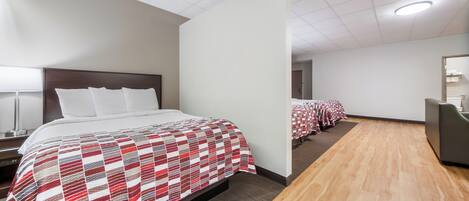 A hotel room with a large bed, a bedside table, a mirror, and a view of the hallway with other rooms.