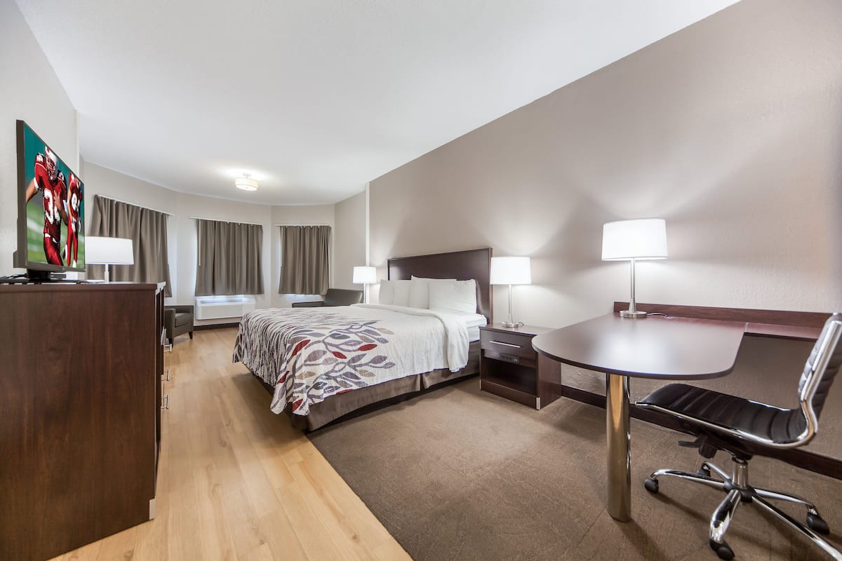 Une chambre d’hôtel comprenant un lit, des tables de chevet, un bureau avec une chaise, une télévision et une lampe.