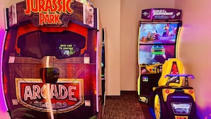 Deux bornes d’arcade, l’une portant l’inscription « Jurassic Park Arcade » et l’autre « Fast & Furious Arcade », se trouvent dans une pièce dont le sol est recouvert de moquette.