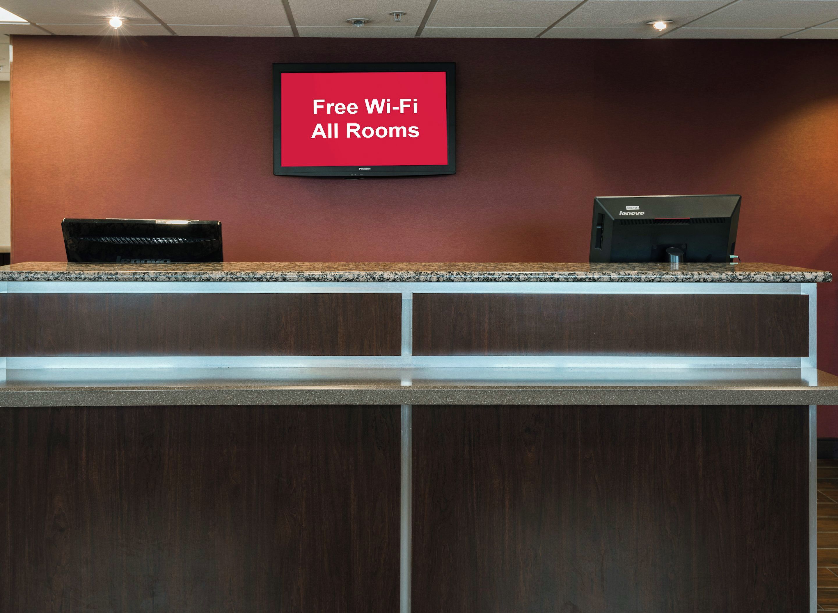 A reception desk with a flat-screen TV displaying 'Free Wi-Fi All Rooms' and a Lenovo computer.