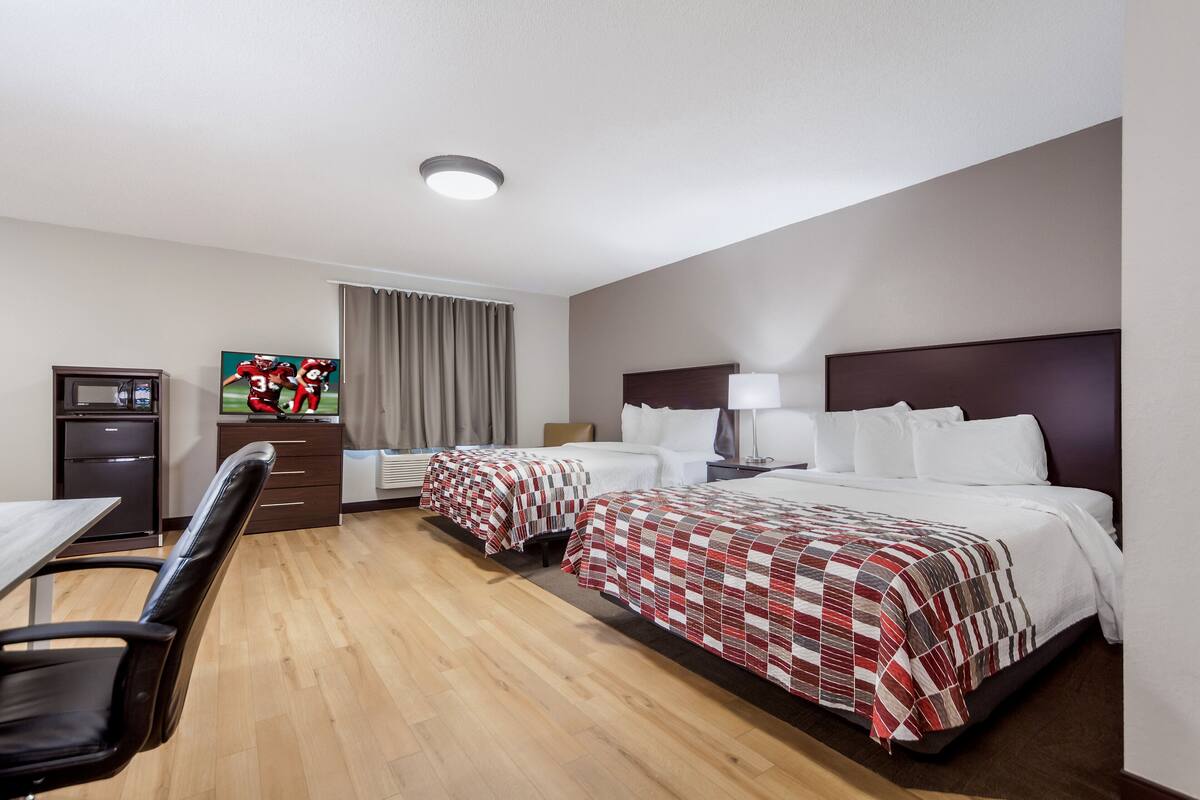 Une chambre d’hôtel avec deux lits, un bureau, une chaise, une télévision et une armoire.