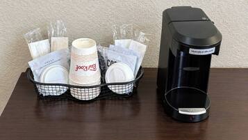 A coffee maker and a basket with disposable cups and napkins on a wooden table.