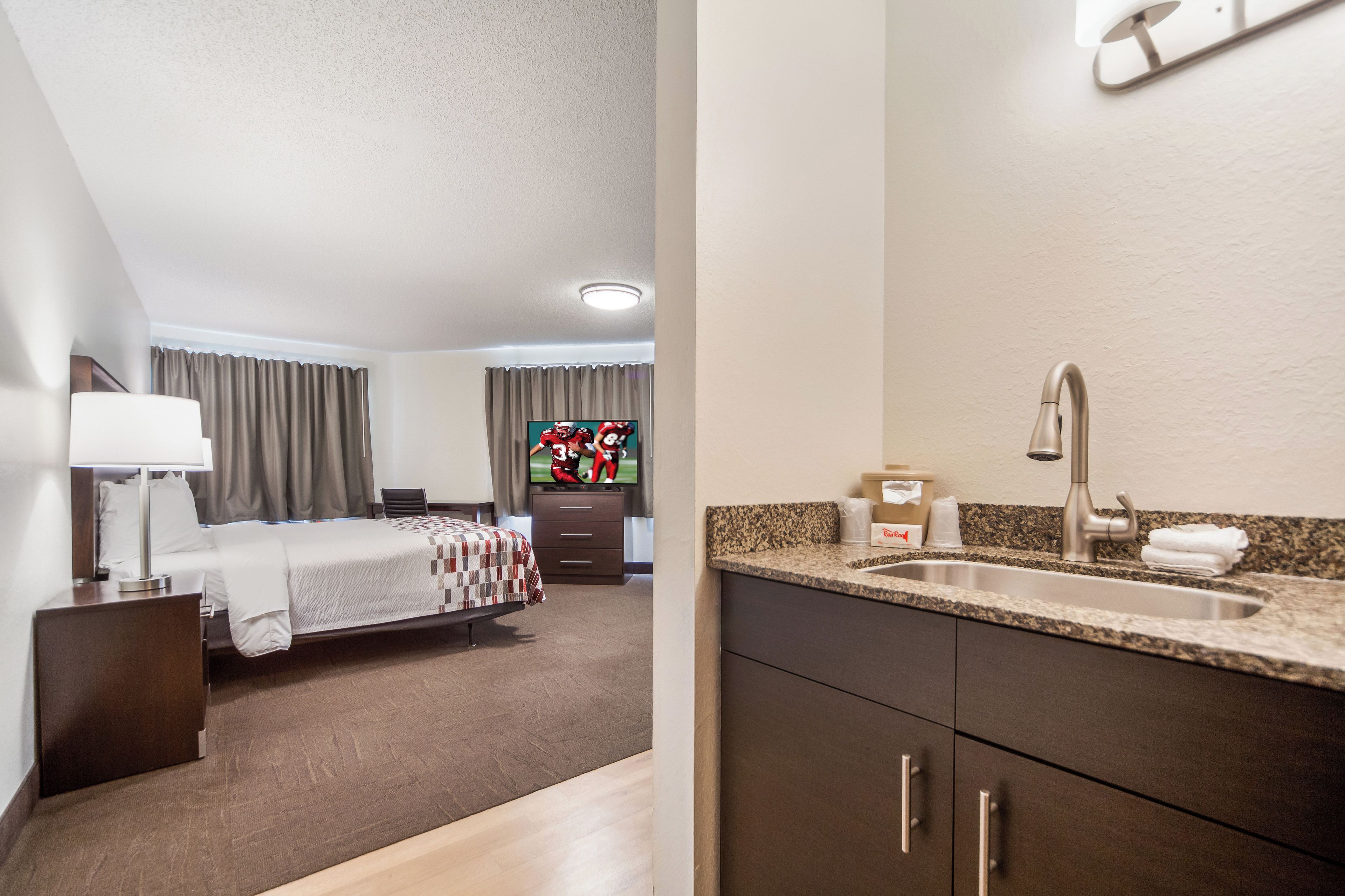 A hotel room with a bed, a desk, a TV, and a bathroom with a sink and cabinets.