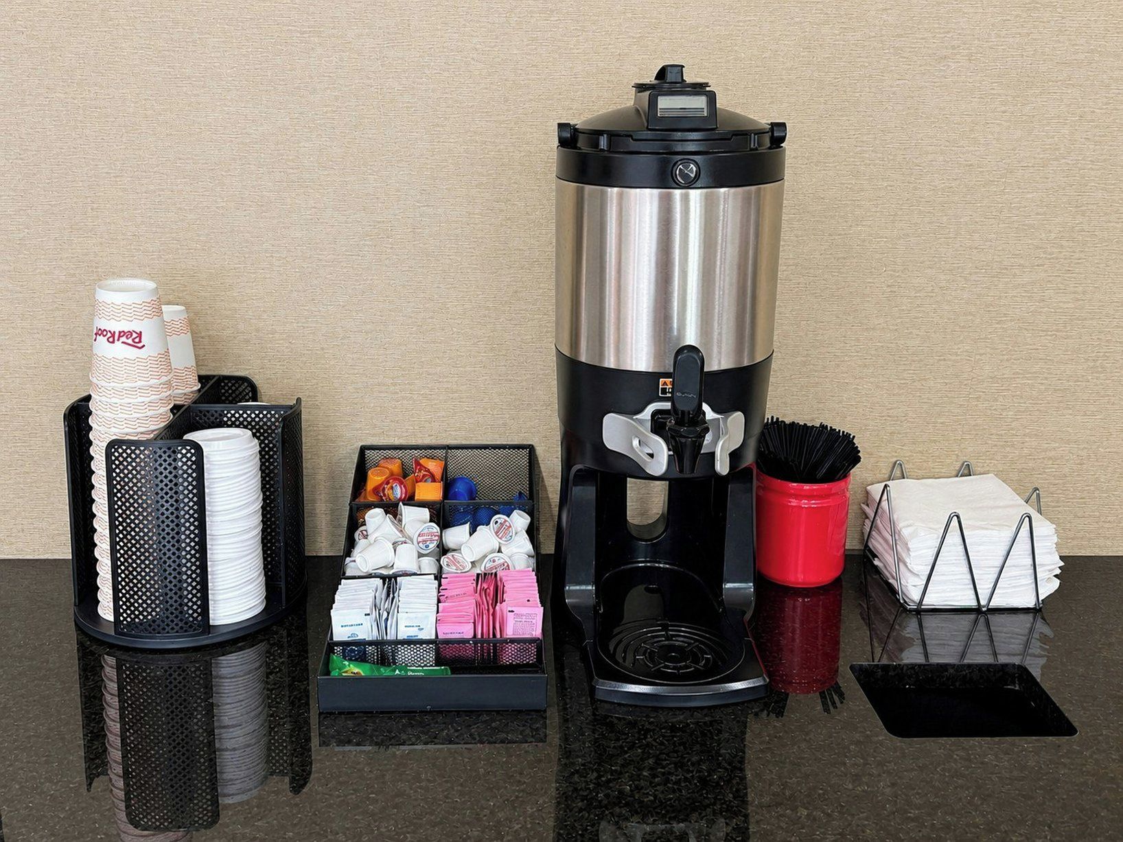 Une machine à café avec un corps en acier inoxydable et un dessus noir, un porte-tasse rouge et une pile de serviettes en papier blanches.