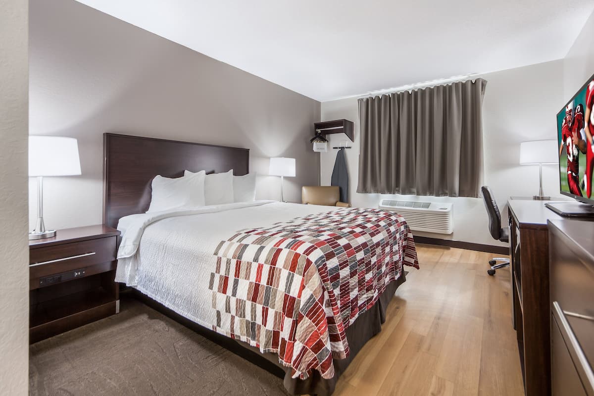 Une chambre d’hôtel avec un grand lit, un bureau, une chaise, une télévision et une fenêtre avec des rideaux.