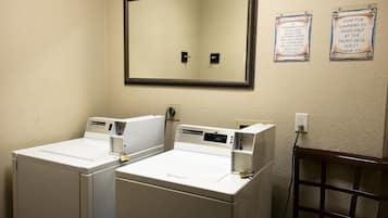 A laundry area with two front-loading washing machines, a mirror, and two informational signs.