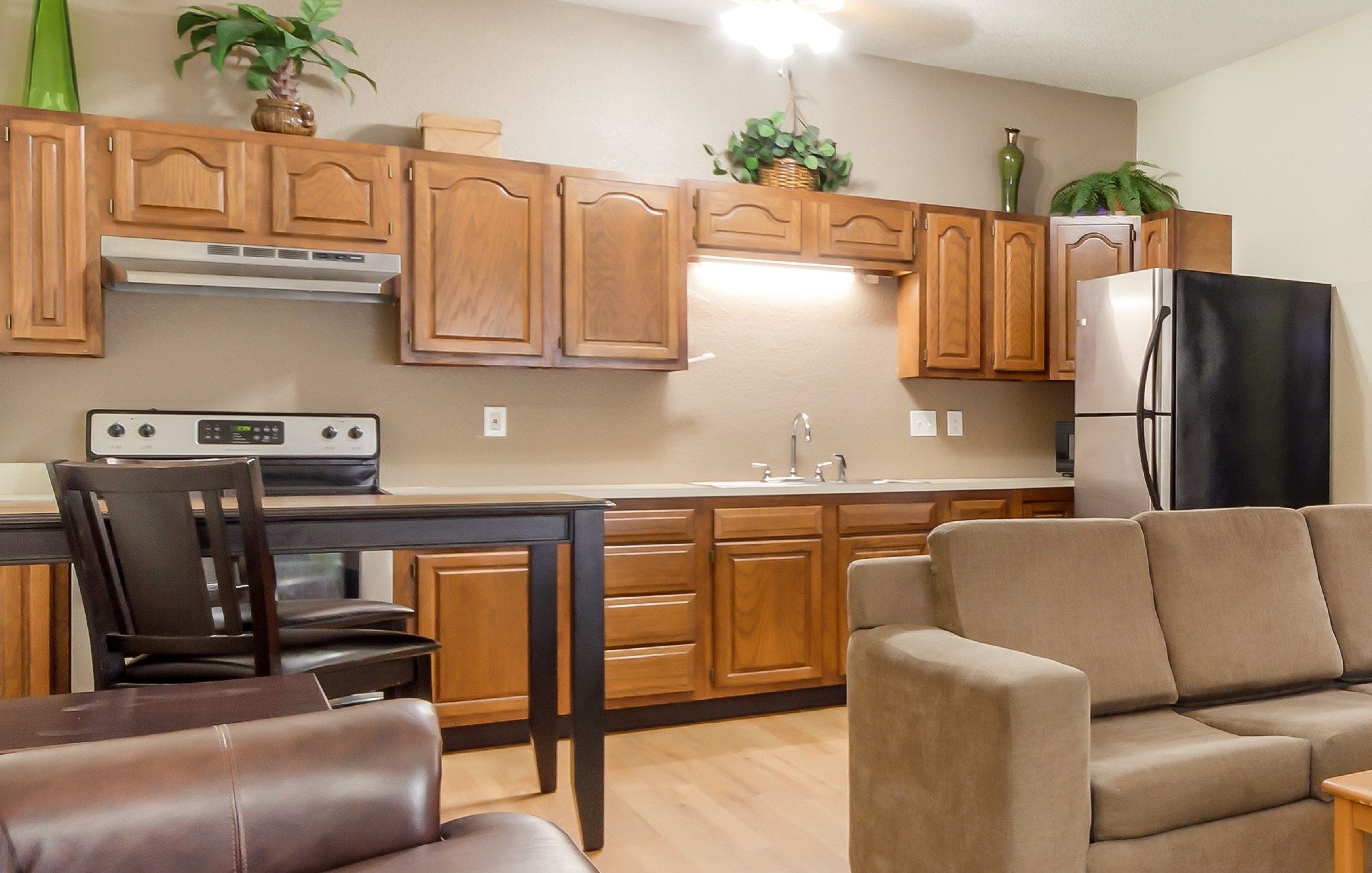 A modern kitchen with wooden cabinets, a built-in oven, a refrigerator, and a dining area with a chair and sofa.