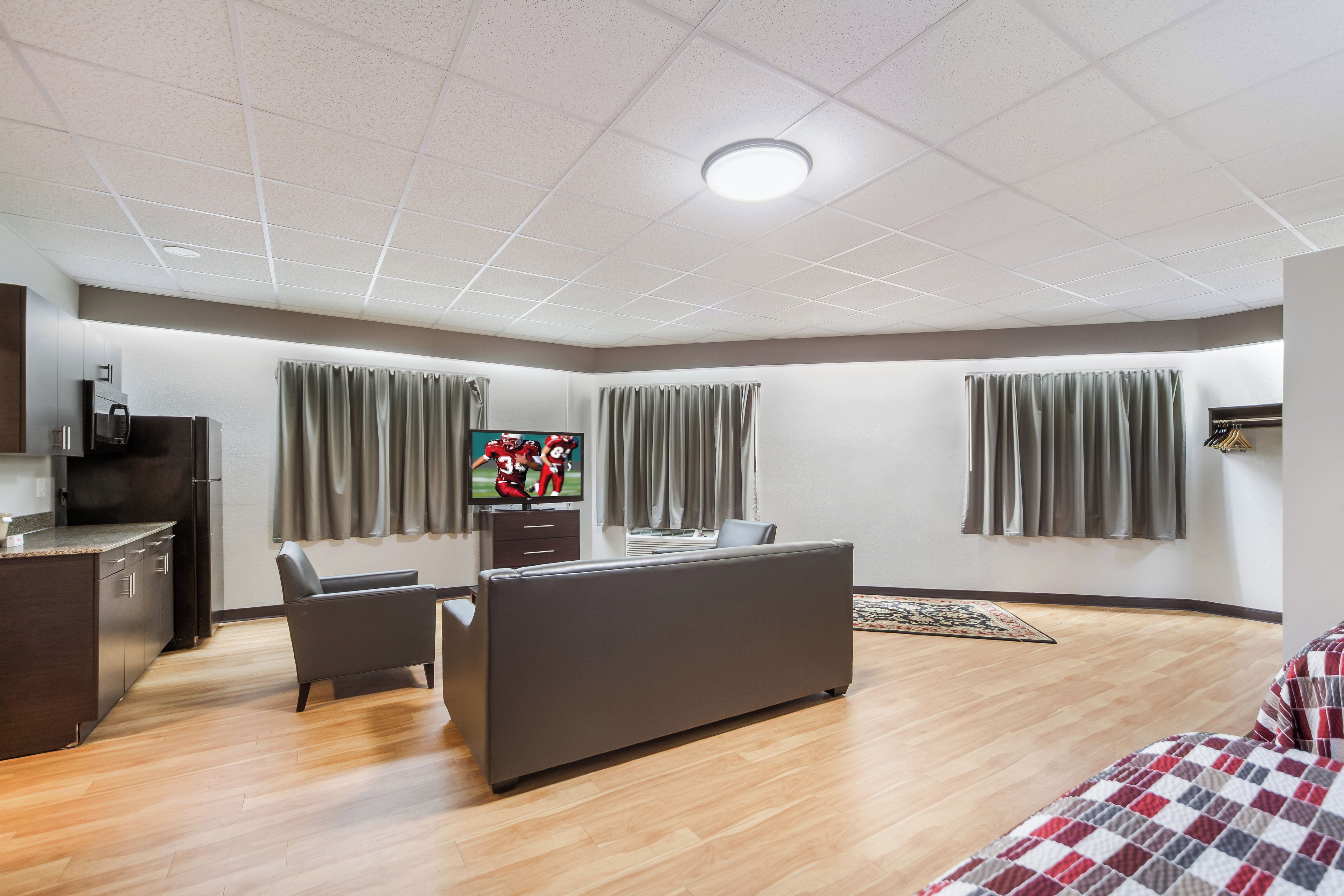 A modern hotel room with a kitchenette, a sofa, a TV, and a bed.