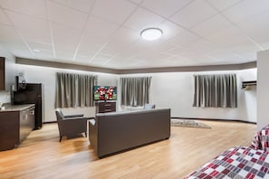 A modern hotel room with a kitchenette, a sofa, a TV, and a bed.
