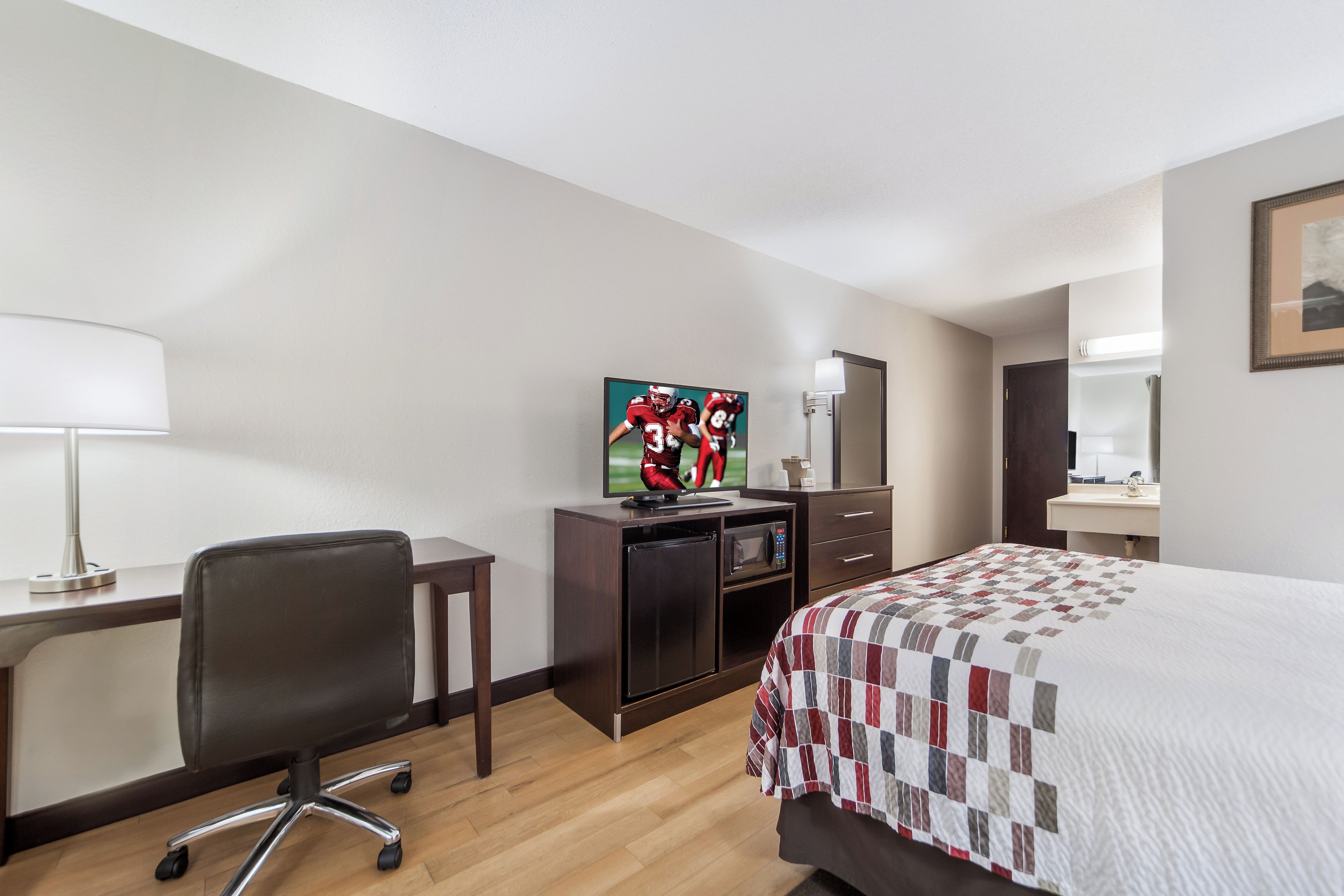 Una habitación de hotel con cama, escritorio, silla, televisor y microondas.