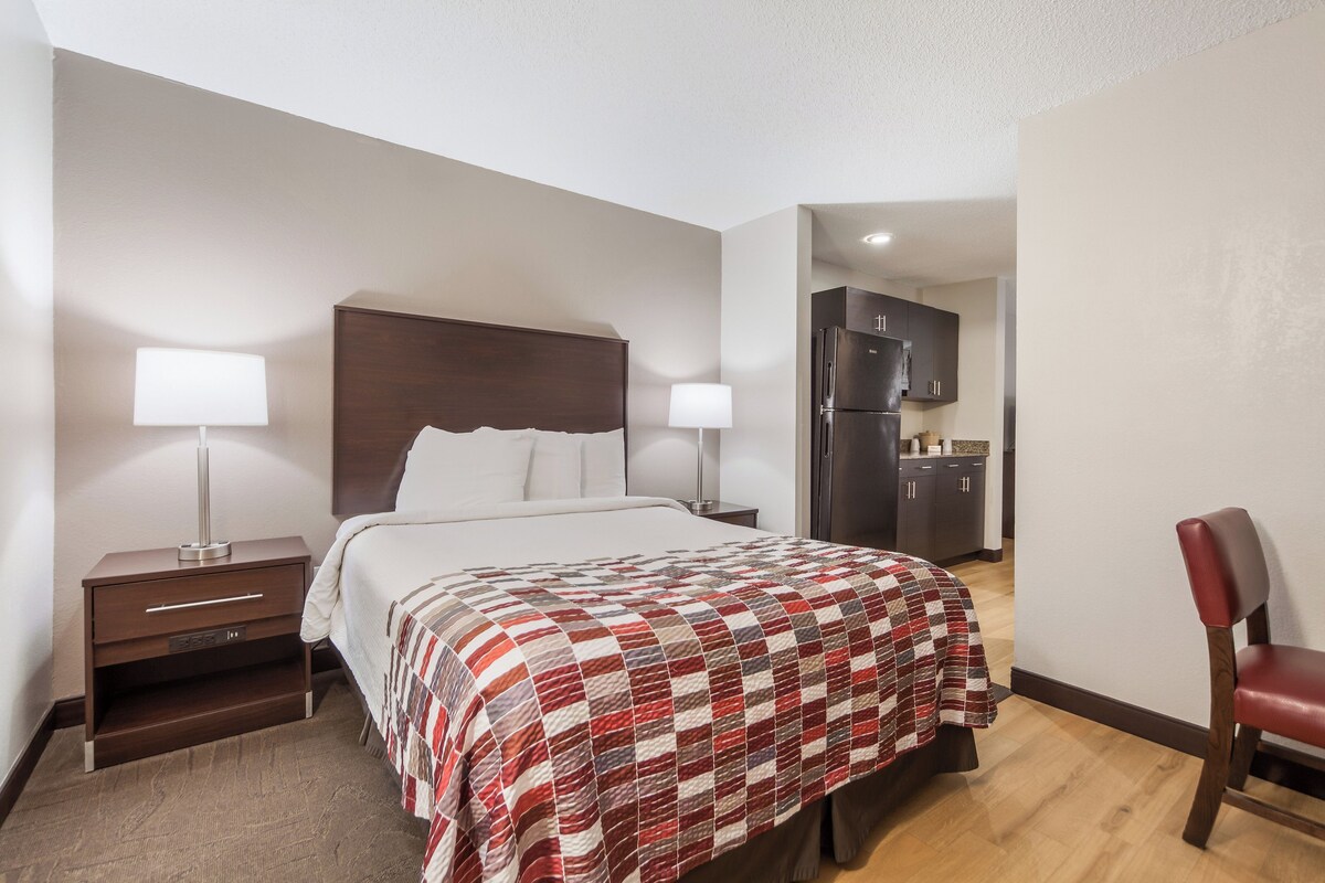 Une chambre d’hôtel comprenant un lit, des lampes de chevet, une chaise, un bureau et une kitchenette.
