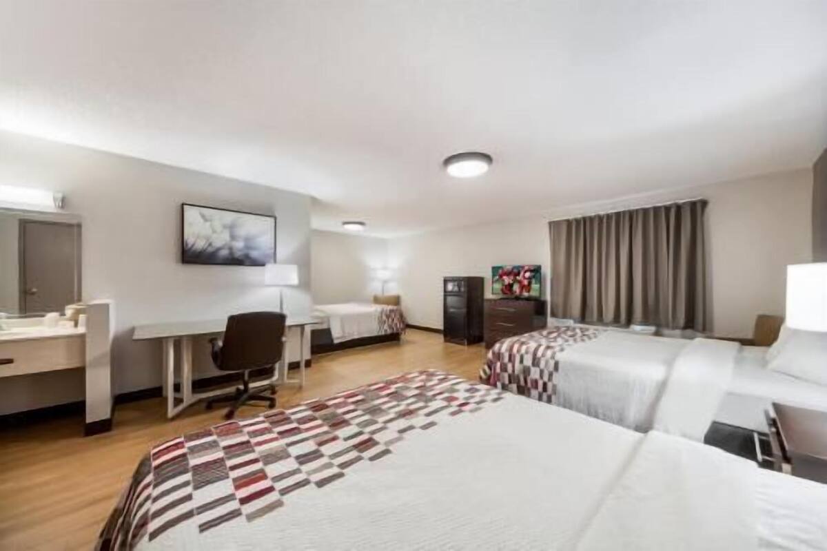 Une chambre d’hôtel avec deux lits, un bureau, une chaise, une télévision et une armoire.