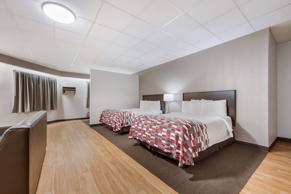Une chambre d’hôtel avec deux lits, un plancher en bois, un luminaire au plafond et une fenêtre avec des rideaux.