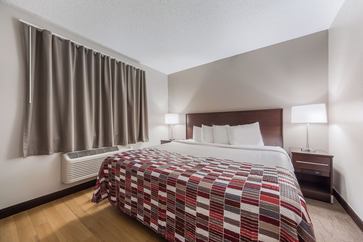 Une chambre d’hôtel avec un lit, des lampes de chevet, un radiateur et une fenêtre avec des rideaux.