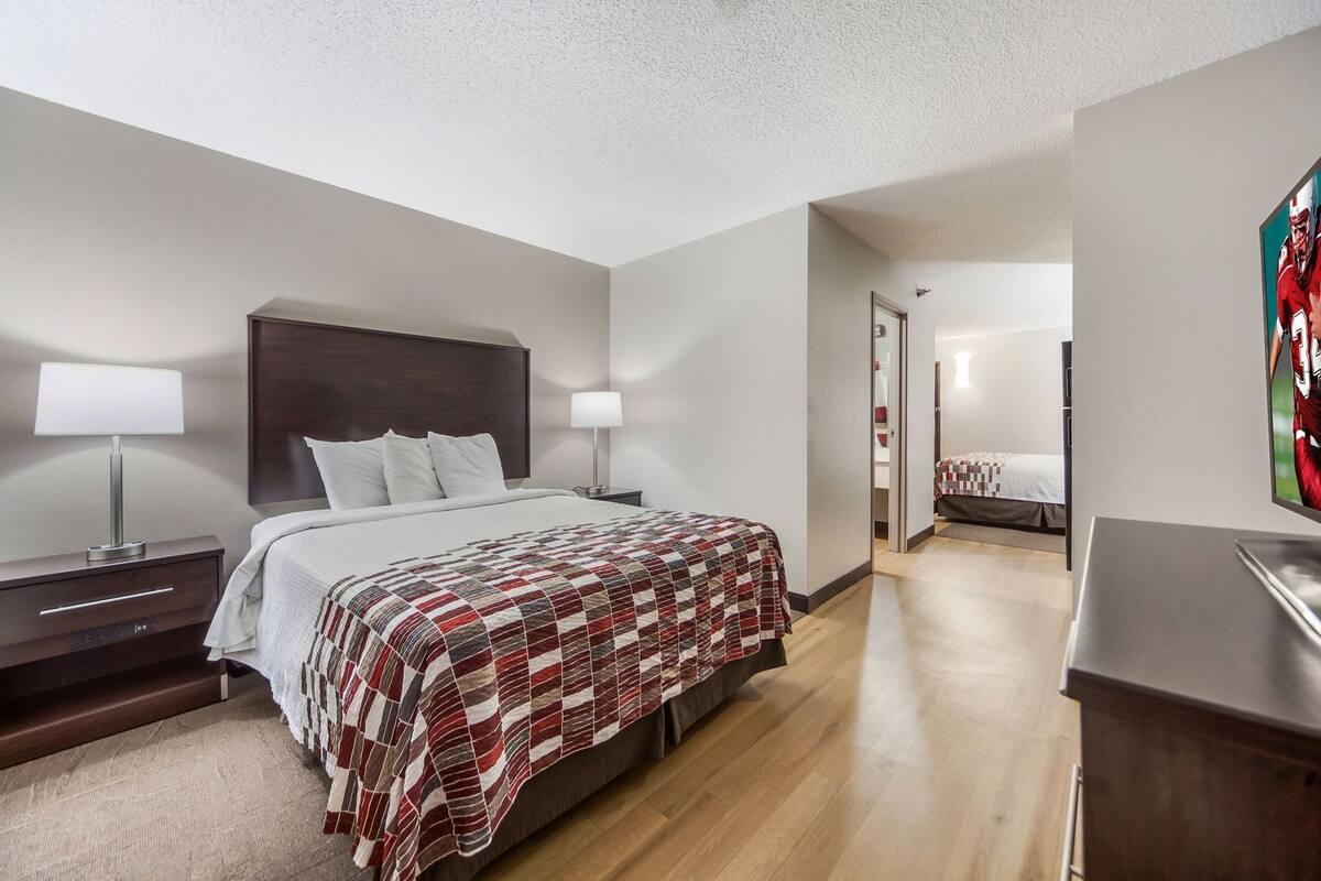 Une chambre d’hôtel avec un grand lit, des tables de chevet avec des lampes, une tête de lit en bois, un petit bureau et un tableau au mur.