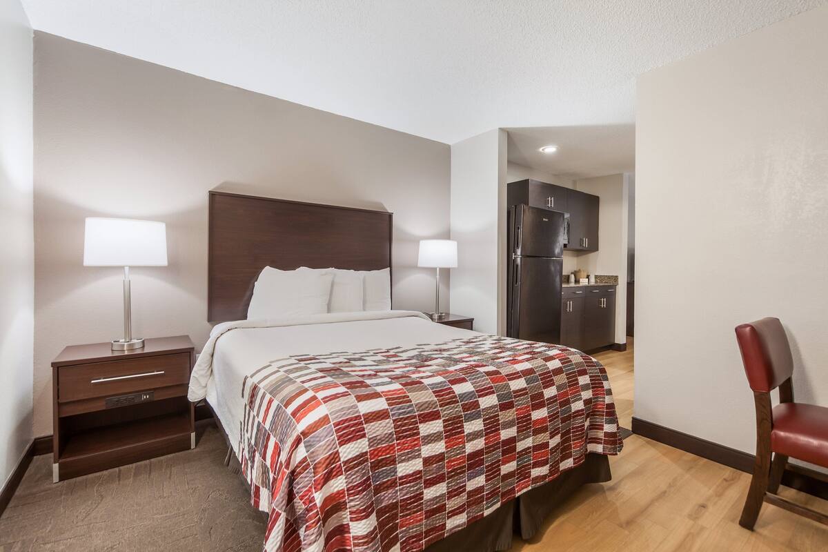Une chambre d’hôtel comprenant un lit, des tables de chevet, une chaise, un bureau et une kitchenette.