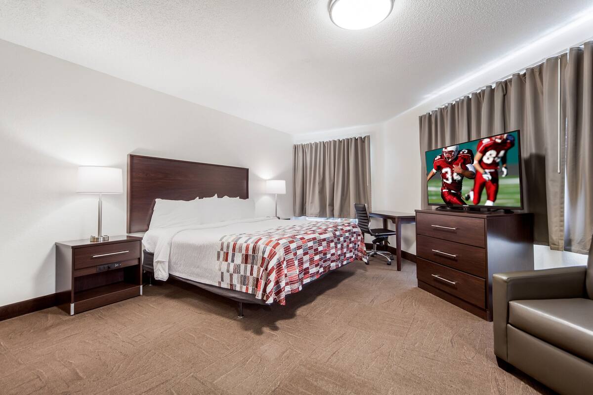 Une chambre d’hôtel avec un lit, un bureau, une télévision et une chaise.