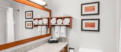 Un baño con lavamanos de encimera de granito, espejo, inodoro y toallero con toallas dobladas.