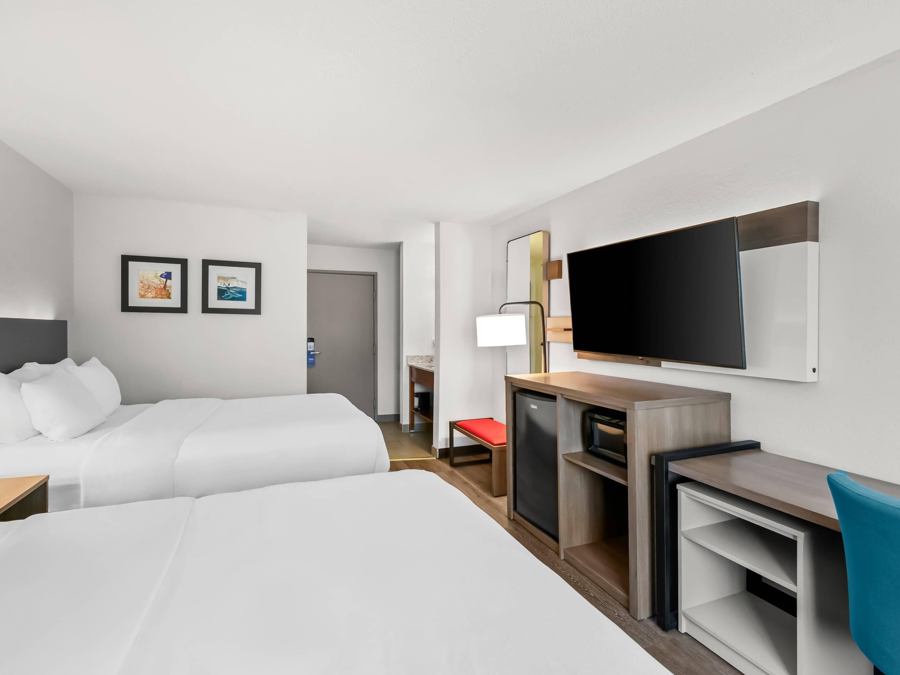 Une chambre d’hôtel avec deux lits, un bureau avec une télévision, une chaise et une petite table.