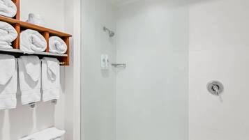 Un baño moderno con cabina de ducha de vidrio, azulejos blancos y un estante de madera con toallas ordenadas.