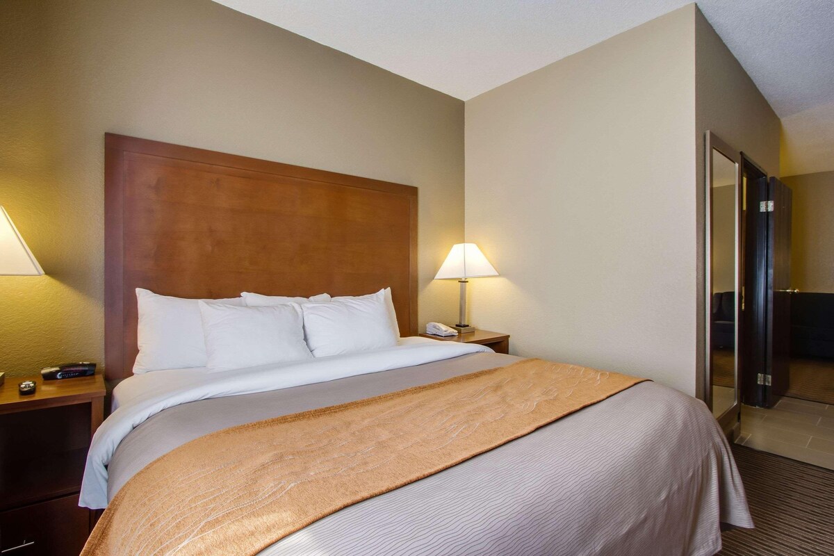 A hotel room with a large bed, two bedside tables with lamps, a wooden headboard, and a door leading to a bathroom.