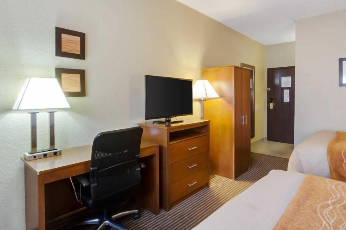 A hotel room with a bed, desk, chair, television, wardrobe, and two lamps.
