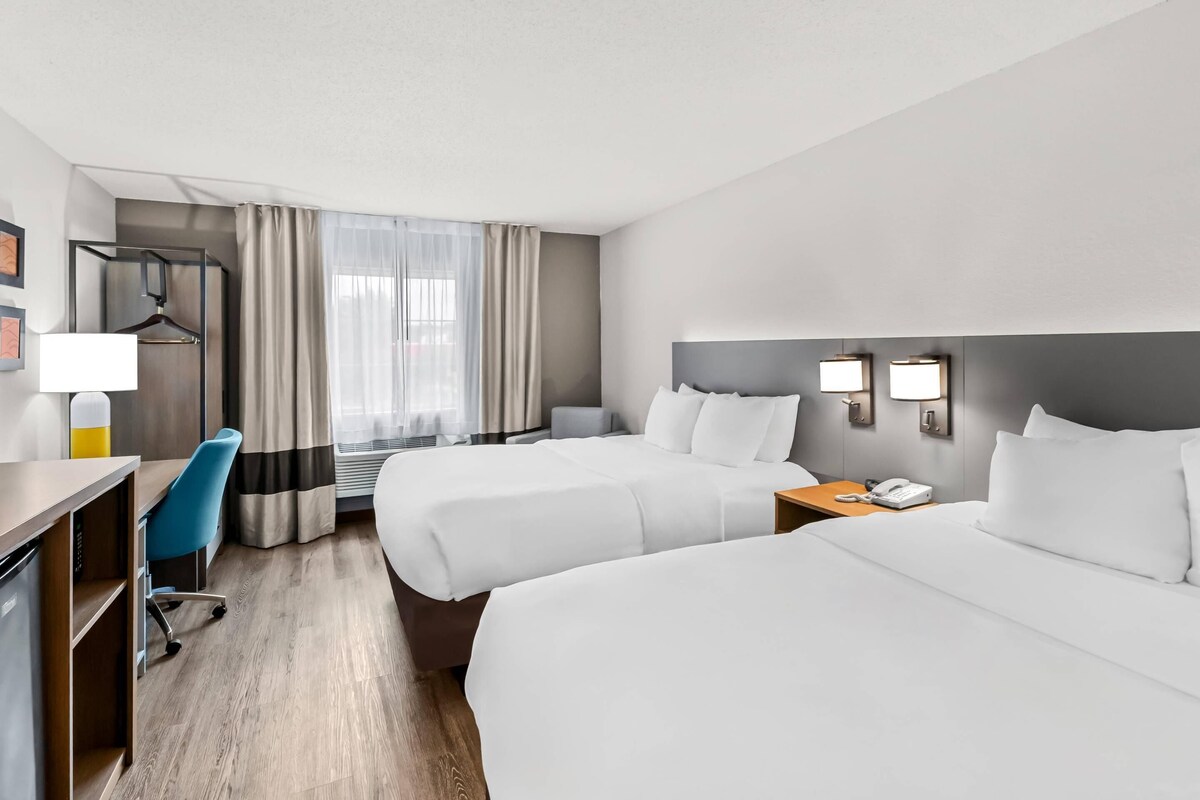 A hotel room with two beds, a desk, a chair, a lamp, a phone, and a window with curtains.