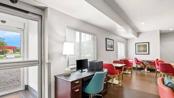 A hotel room with a desk, computer, and red chairs.