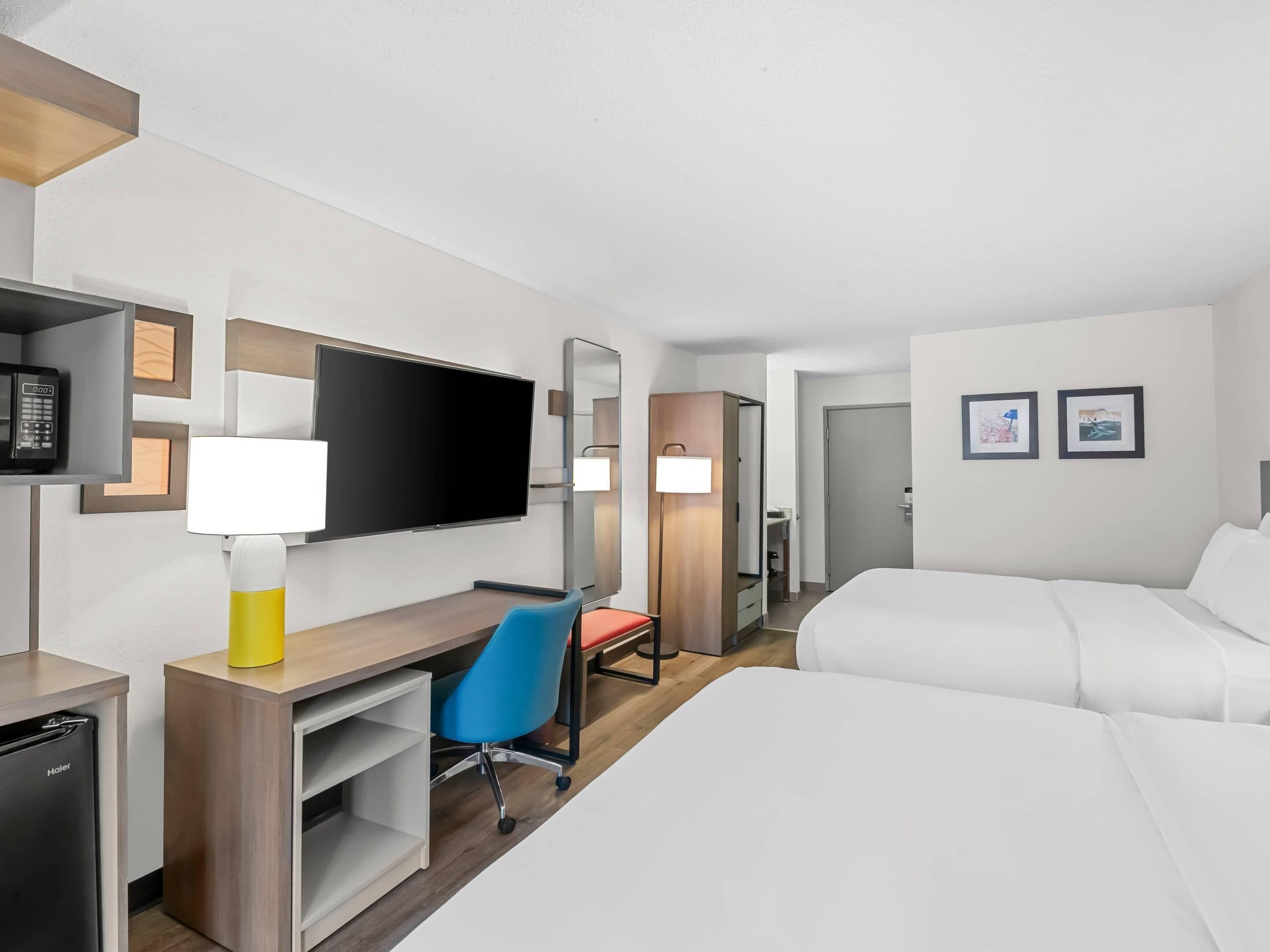 Habitación de hotel con cama, escritorio con silla, televisión, espejo y armario.
