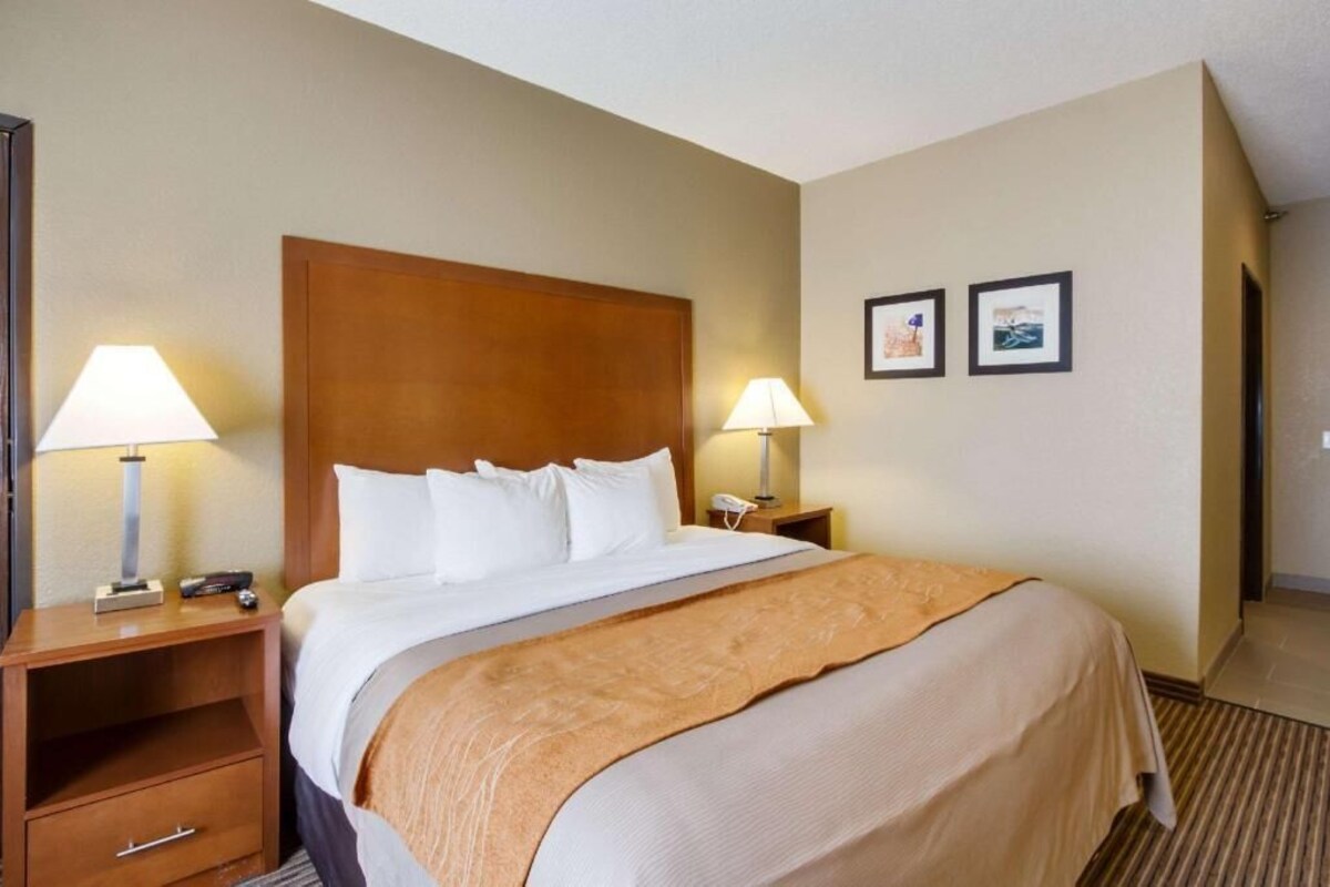 A hotel room with a large bed, two bedside lamps, a wooden headboard, a nightstand with a phone, and two framed pictures on the wall.