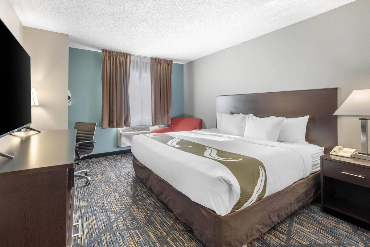 A hotel room with a bed, desk, chair, and a television.
