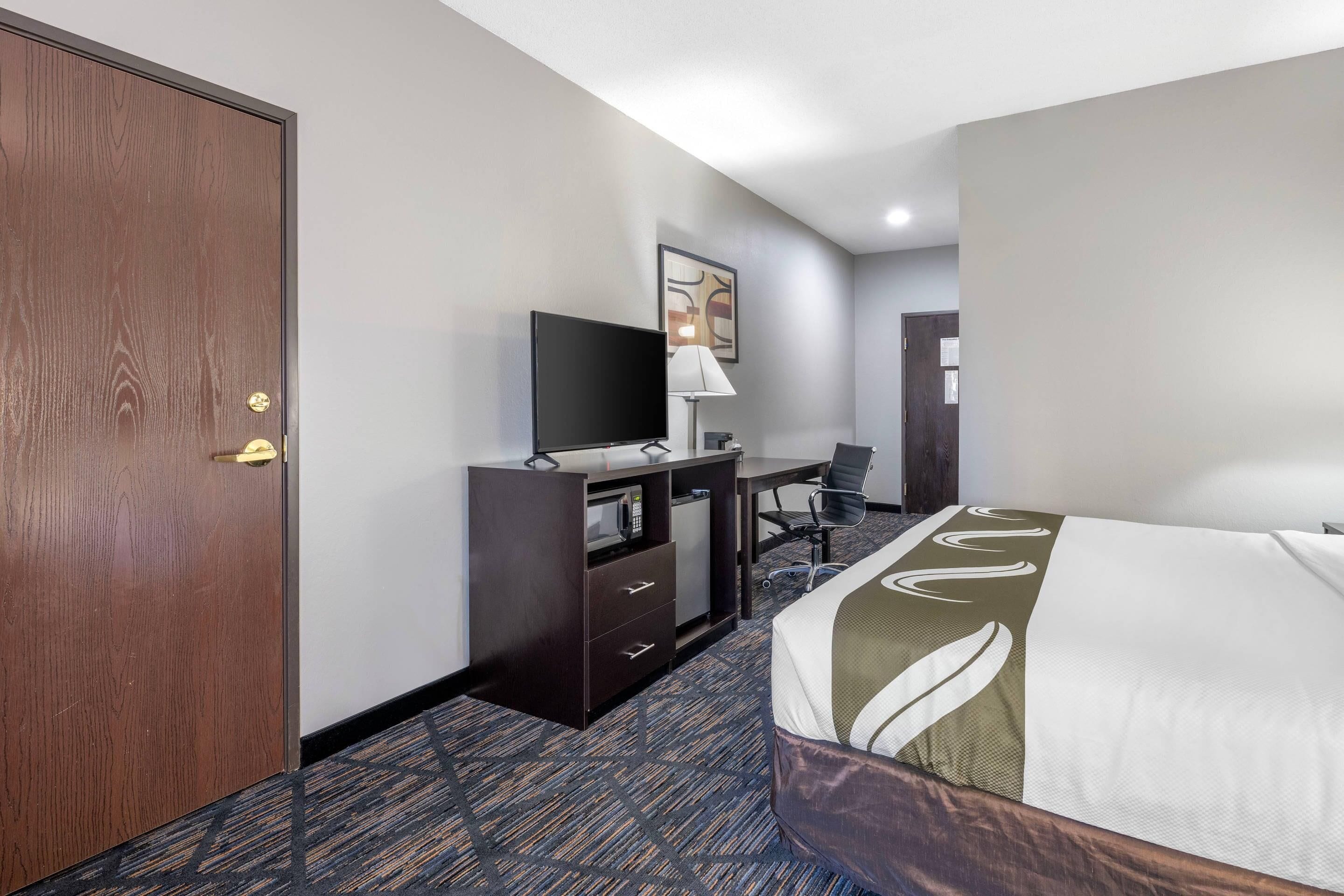 A hotel room with a bed, a desk with a computer, a television, and a wardrobe.