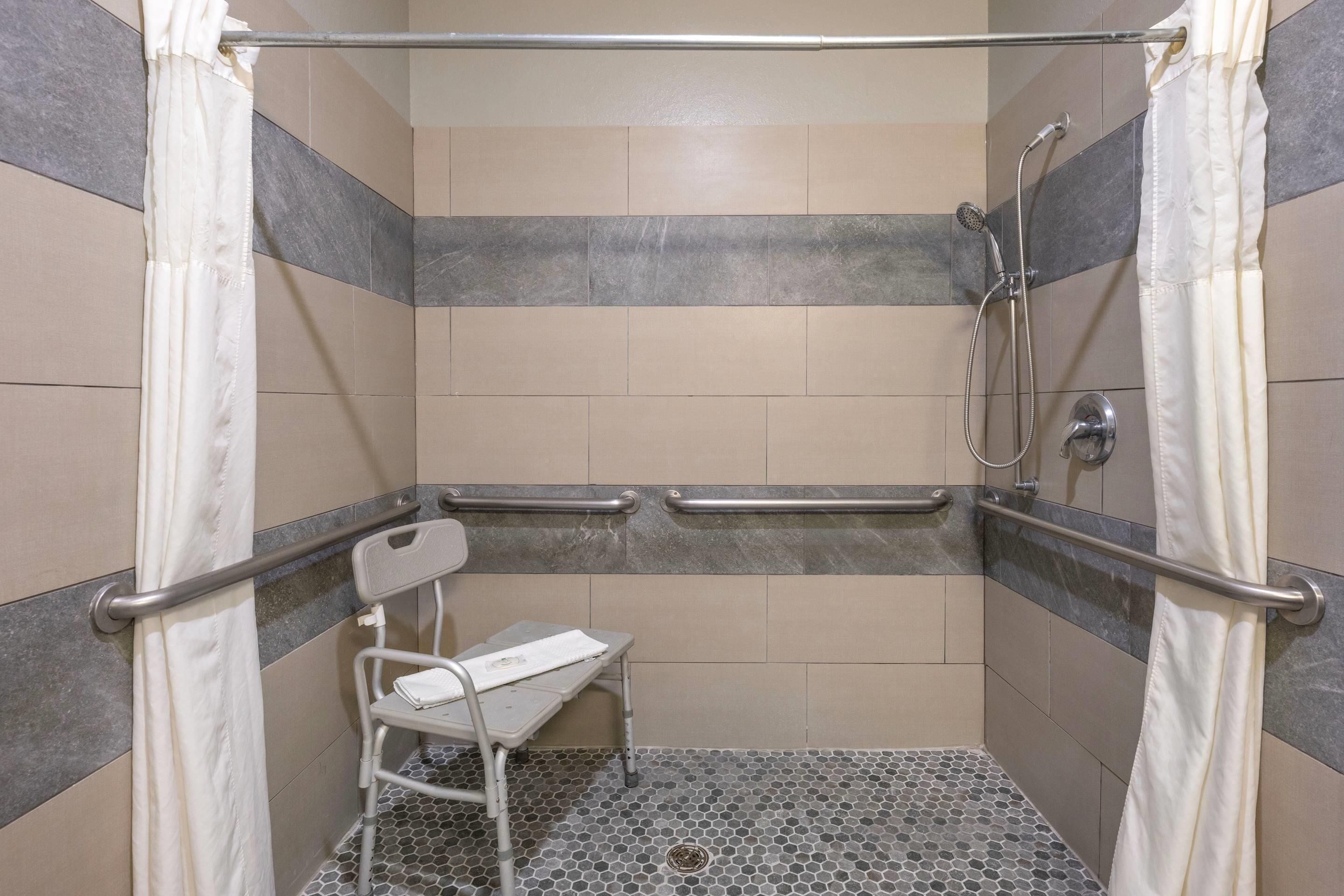 A shower area with a grab bar, a wheelchair-accessible bench, and a showerhead.