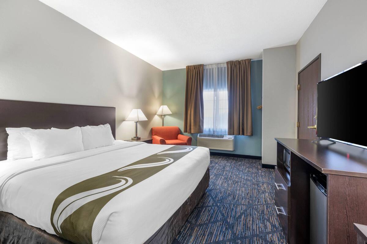 A hotel room with a large bed, two bedside lamps, a TV, a desk, and a chair.