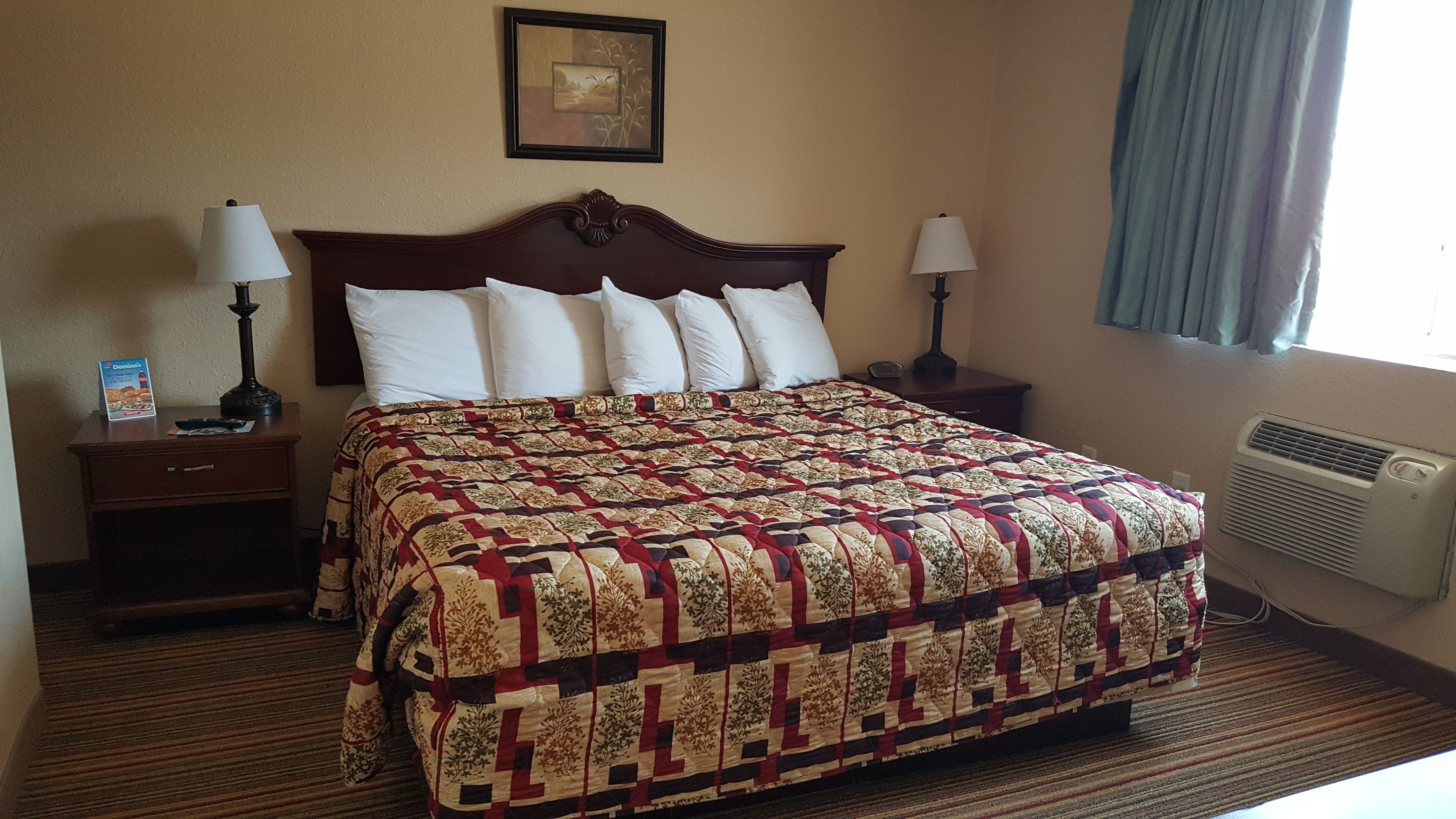 A hotel room with a large bed, two bedside tables with lamps, a framed picture on the wall, and a window with curtains.