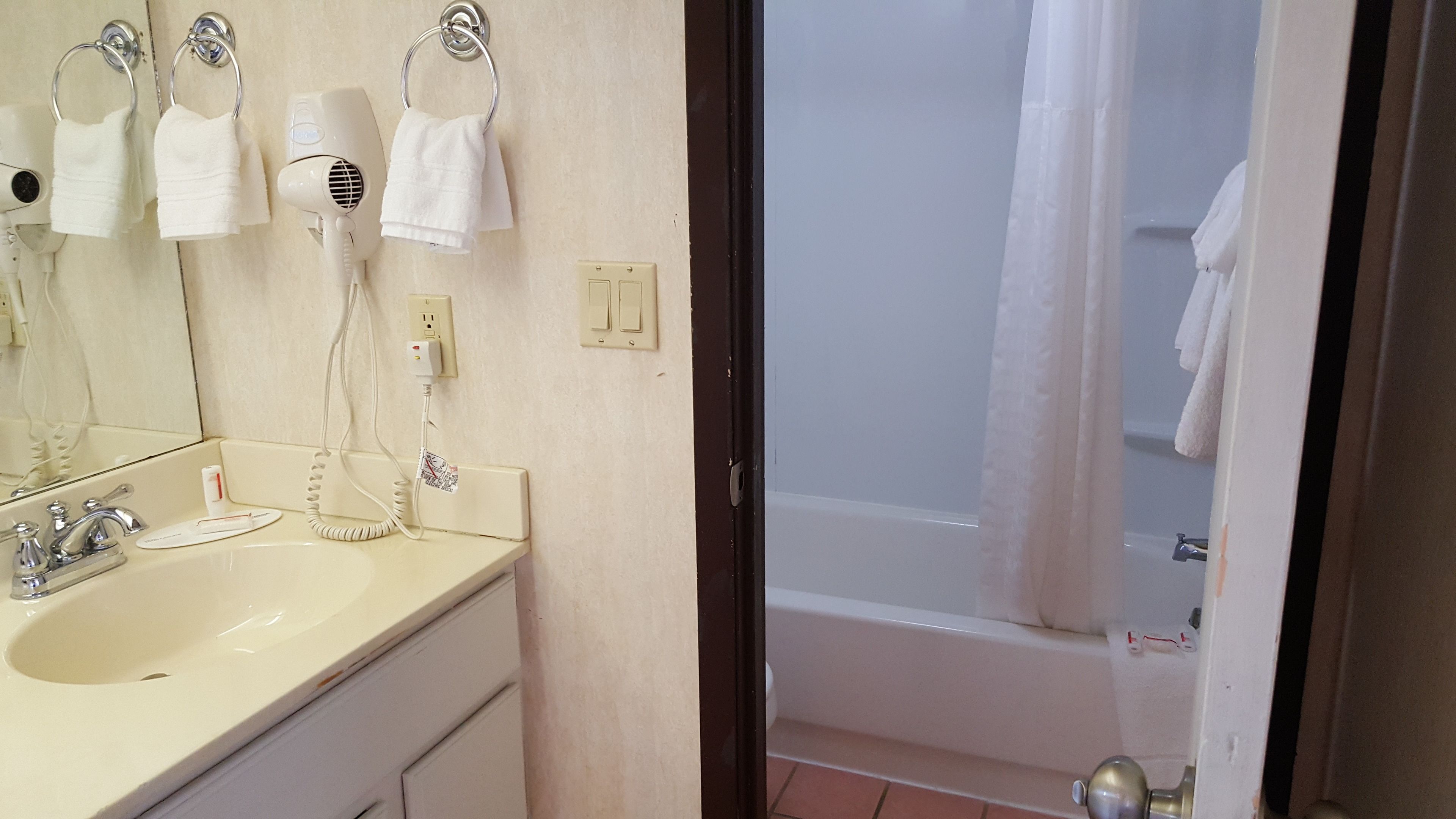 A bathroom with a sink, two hair dryers, a towel rack, and a shower curtain.