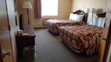 Habitación de hotel con dos camas, un escritorio con lámpara, un cubo de basura y una ventana con cortinas.