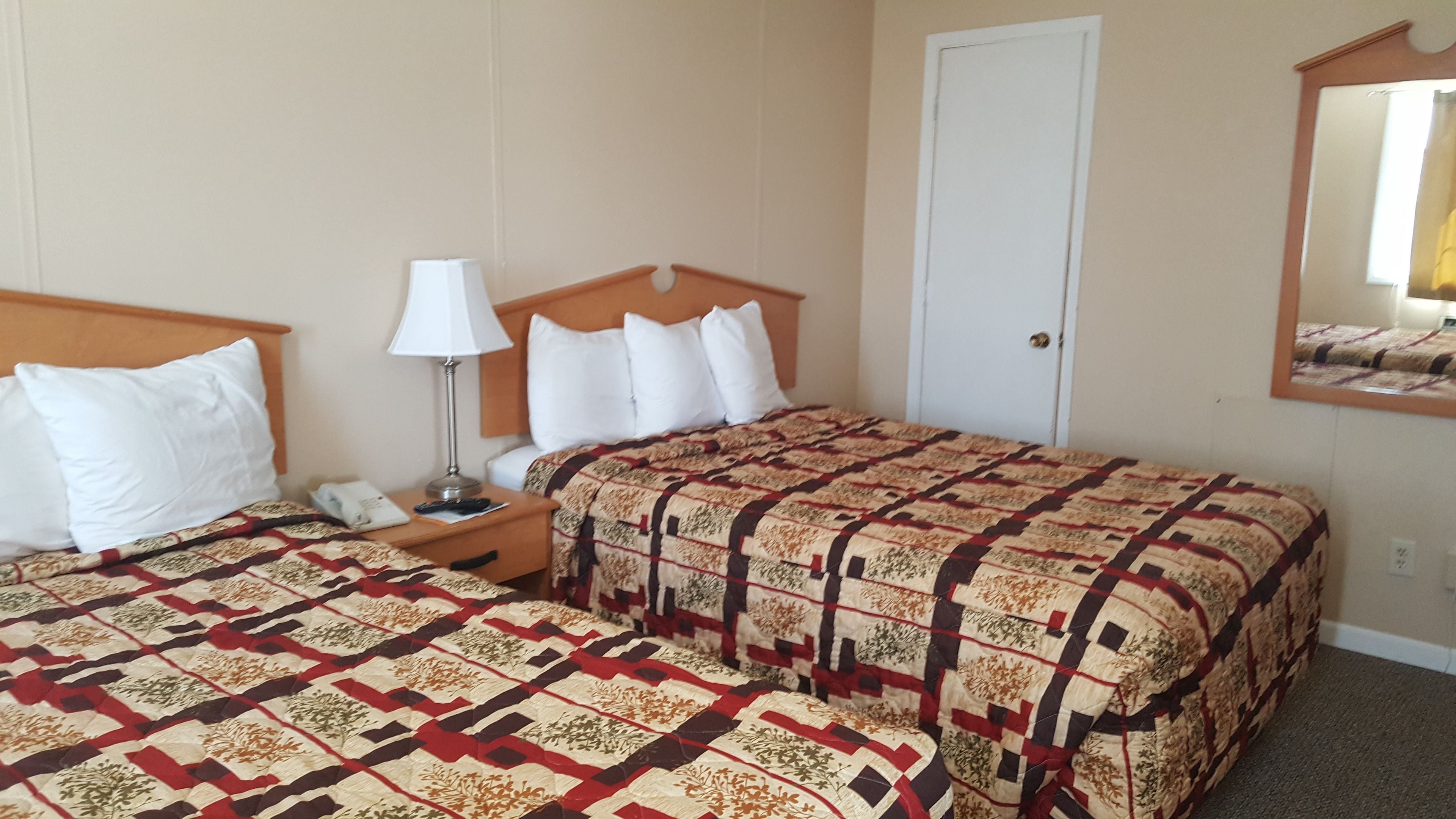 A hotel room with two beds, a nightstand, a lamp, a door, and a mirror.