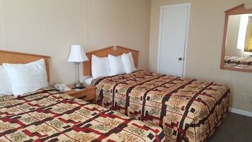 A hotel room with two beds, a nightstand, a lamp, a door, and a mirror.