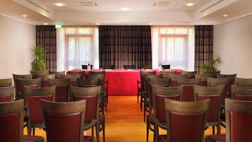 Una sala conferenze con file di sedie di legno e un tavolo rosso in prima fila.