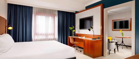 Una habitación de hotel con una cama grande, un escritorio con una silla, un televisor y una mesita con una planta.