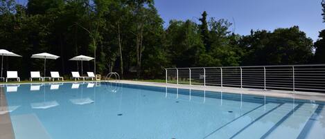A clear blue swimming pool with white lounge chairs and umbrellas, surrounded by trees.
