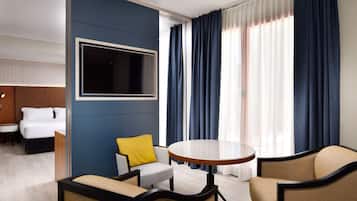 A hotel room with a bed, a desk, a chair, a round table, and a large window with curtains.