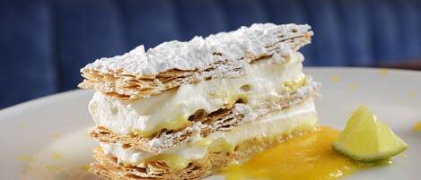 A dessert with multiple layers of pastry and cream, garnished with a mint leaf and a slice of lime.