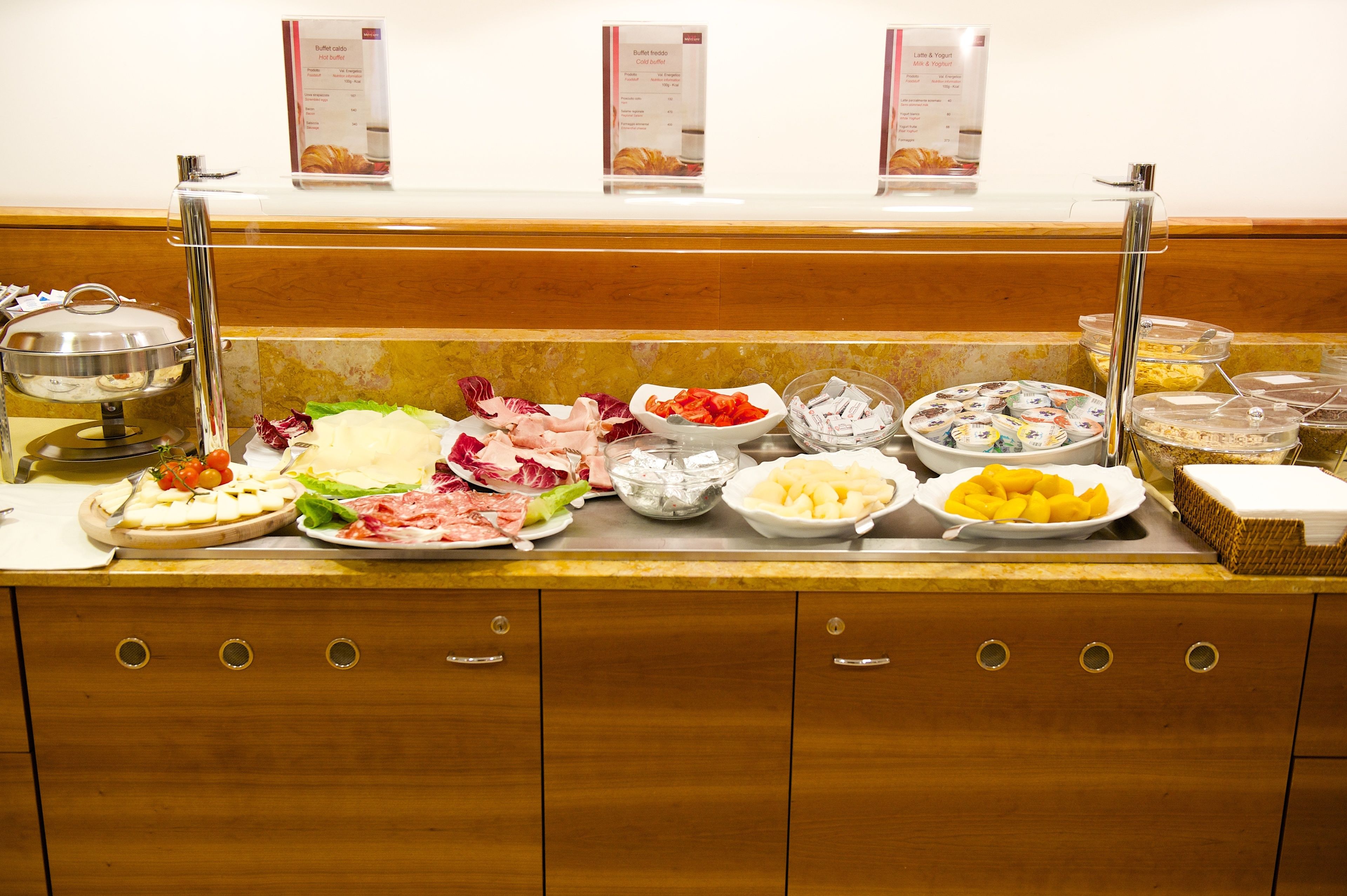 Un banco buffet con diverse pietanze, tra cui carni, formaggi e frutta.