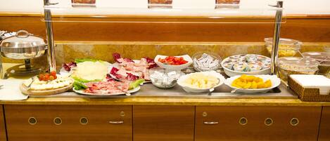 Un banco buffet con diverse pietanze, tra cui carni, formaggi e frutta.
