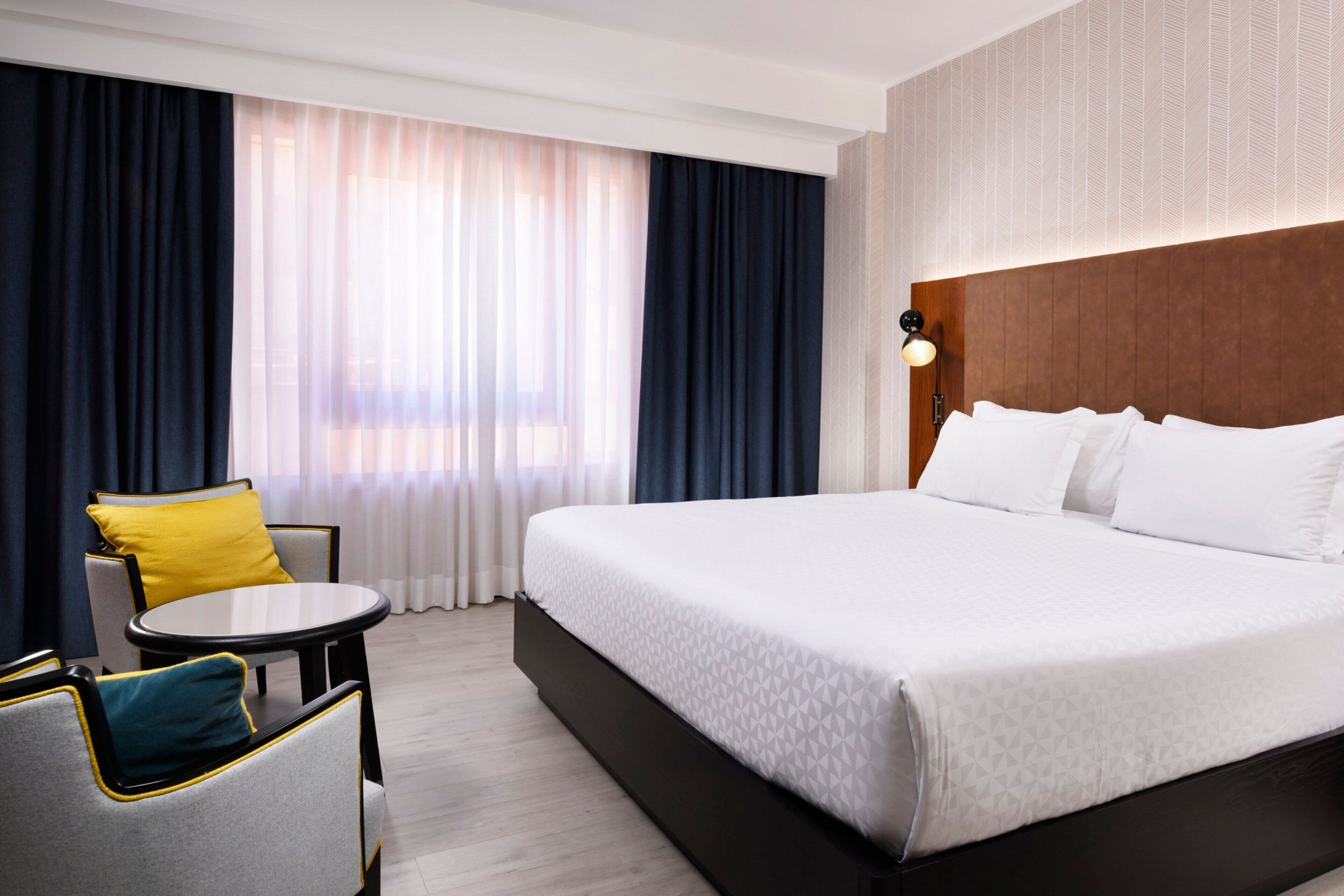 A hotel room with a large bed, a round table, and two chairs.