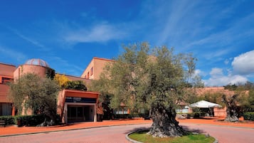 A hotel entrance with a four-point logo, a large tree, and a clear blue sky.